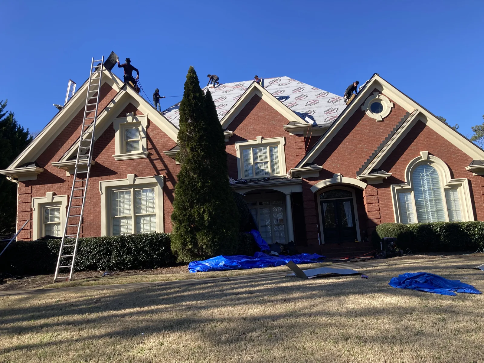 Roofing installation on a large brick home, viewed from the front